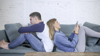 Wall Mural - young attractive couple in relationship problem with internet mobile phone addiction girlfriend ignoring sad neglected and bored boyfriend at home