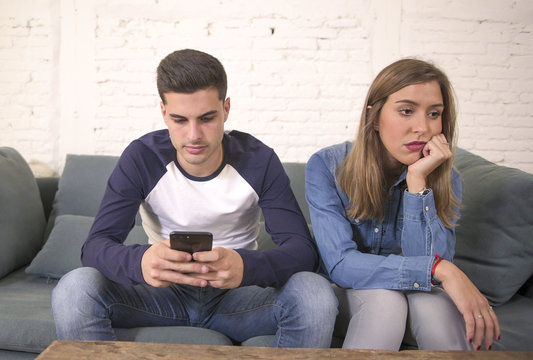young attractive couple in relationship problem with internet mobile phone addiction boyfriend ignoring sad neglected and bored girlfriend