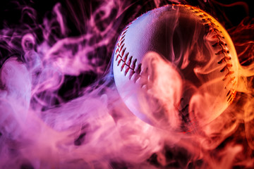 Close up of a white baseball ball in multi-colored red smoke from a vape on a black isolated background