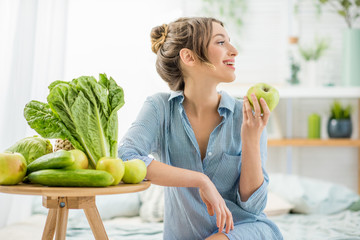 Wall Mural - Portrait of a young and beautiful woman sitting with healthy green and fresh food indoors in the bright living room with green plants at home