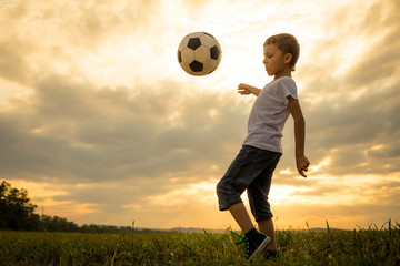 Young little boy playing in the field  with soccer ball.