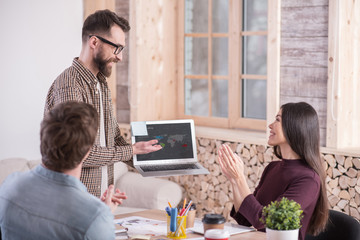 Wall Mural - My project. Nice smart delighted man standing in front of his colleagues and holding a laptop while presenting a project