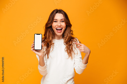 Fotomural Happy brunette woman in sweater showing blank smartphone screen