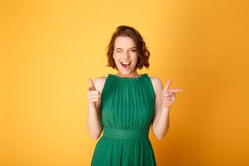 portrait of winking woman pointing at camera isolated on orange