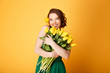 portrait of smiling woman with bouquet of yellow tulips in hands isolated on orange