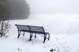 Fototapeta Most - A bench at the edge of snow-covered field on foggy morning - winter scenery