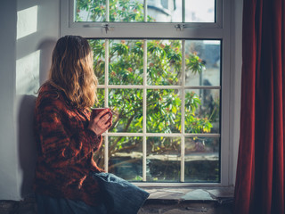 Wall Mural - Young woman drinking tea by the window