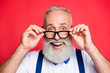 © deagreez - Portrait of cheerful, glad, confident, professional barber looking out glasses, holding eyelet of spectacles on face with two hands, with wondered expression, open mouth, isolated on red background
