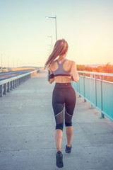 Back view of sporty girl running over the bridge.