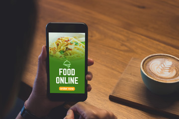 Poster - Close up woman hand holding food online mobile apps with hot coffee cup on table sitting at coffee shop,online order concept.