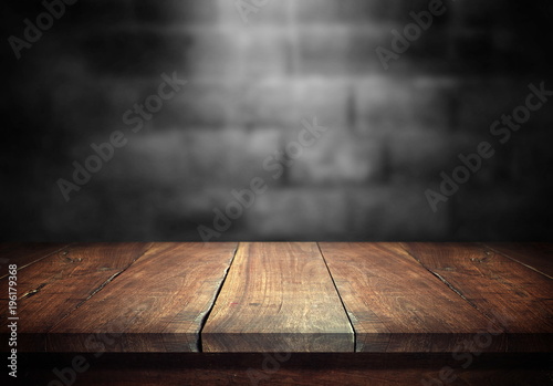 Cuadros en Lienzo Old wood table with blurred concrete block wall in dark room background