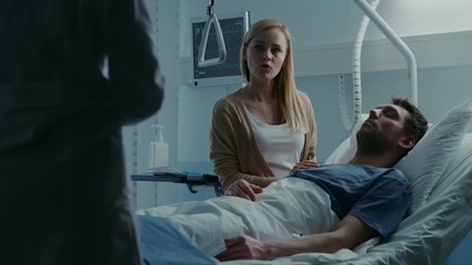 Wall Mural - In the Hospital, Patient Lying in Bed, his Wife Sitting Beside the Sick Man Listens to Doctor's Explanations. Love and Care Concept. Shot on RED EPIC-W 8K Helium Cinema Camera.