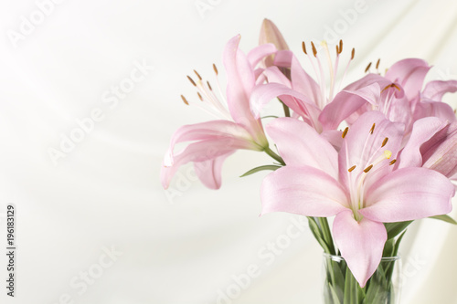 Plakat Piękna różowa leluja w szklanej wazie na białej tkaninie