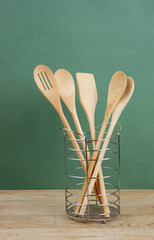 Wall Mural - wooden kitchenware in metal basket on old wooden table over green background