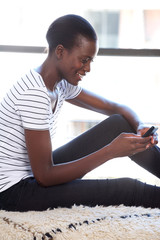 Wall Mural - Happy young black woman using cellphone by window indoors