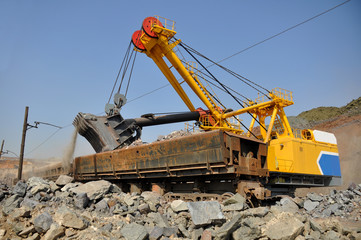 A large yellow excavator loads ore into a railway car