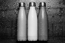 Stainless Thermos Bottles On A Wooden Table Sprayed With Water. Black And White.