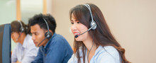 Close Up Focus On Asian Call Centre Woman With Team Working By Talking On Headphone Trying To Response Answer Or Working In Operation Office Room.helpdesk Hotline Concept.