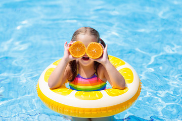 Wall Mural - Child in swimming pool. Kid eating orange.