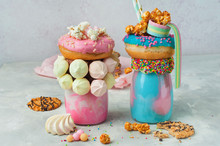 Two Freak Shakes Topping With Donut, Marshmallow, Popcorn And Marmalade On Grey Background