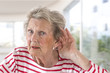 © JPC-PROD - Elderly lady with hearing problems due to ageing holding her hand to her ear as she struggles to hear, profile view on large windows background