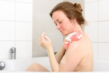Mature Caucasian Woman (47) Having A Bath In Her Bathtub. She Uses A Pink Bath Sponge To Clean Her Upper Body.