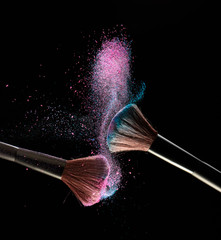 Make-up brushes with pink and blue powder explosion on black background