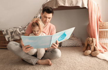 Wall Mural - Father with little daughter reading bedtime story near hovel at home