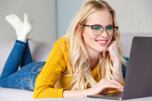 Beautiful Smiling Young Woman In Eyeglasses Lying And Using Laptop