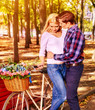 Walking bike of couple in park and kissing. Summer friends walk outdoor. First date of two young people in good weather day. Sun backlight on background. Love at first sight. Sun flare first love of