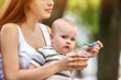 Baby feeding spoon by mother in park outdoor. Weaning in first weeks. Portrait of happy beautiful mom and eating child summer on bench. Good appetite fresh air by baby food. Vitamins for kid.