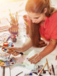 Authentic artist children girl paints with set palette watercolor paints palette and brush in morning sunlight. Sun flare private business in drawing for student. Indoor home interior handmade crafts.