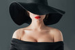 woman in black hat with red lips, on gray background, selective focus. Elegance and feminine sensuality