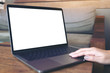 © Farknot Architect - Mockup image of a hand using and touching laptop with blank white desktop screen on wooden table in cafe