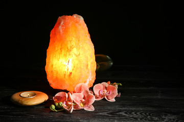 Wall Mural - Himalayan salt lamp, candle and flowers on table against dark background