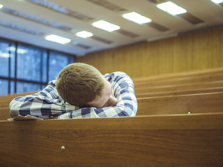 young student in checkered shirt sleeping in the empty lecture hall