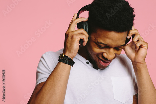 Fényképezés Portrait of a cool young guy listening to music with headphones on pink backgrou