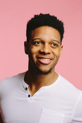 Wall Mural - Portrait of a smiling African American guy looking to the side and up  on pink background