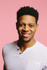 Wall Mural - Close up of a cool smiling African American guy in white shirt on pink background