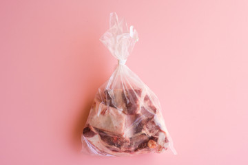 Directly above view of meat in plastic bag on pink background