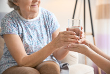 Caregiver Giving Glass Of Water To Senior Woman At Home, Closeup