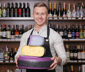 Wall Mural - Young worker holding different cheeses in shop