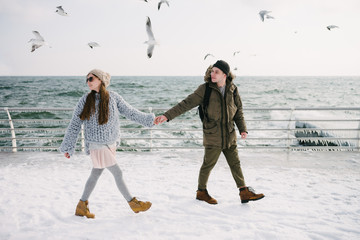 Wall Mural - stylish couple holding hands and walking on winter quay at sea with seagulls