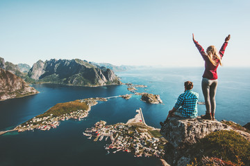 Wall Mural - Couple family traveling together on cliff edge in Norway man and woman lifestyle concept summer vacations outdoor aerial view Lofoten islands Reinebringen mountain top