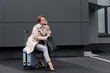 © LIGHTFIELD STUDIOS - businesswoman in stylish coat sitting on suitcase while waiting for taxi on street