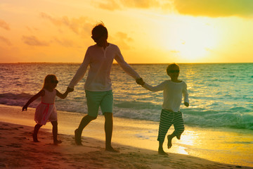 father with two kids play on beach at sunset