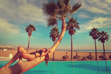 Wall Mural - woman lying on pool bent palm tree trunk