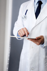 Male doctor working on a digital tablet near a window