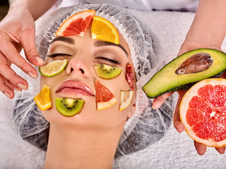 Facial mask from fresh fruits for woman. Beautician apply slices of avocado, grapefruit. Removal of pigmented spots. Top view.