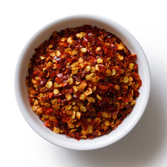 Poster - Coarsely ground chilli peppers in white ceramic bowl isolated on white from above.